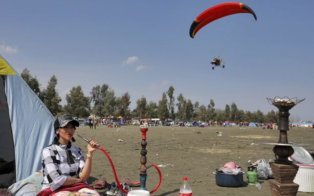 Una mujer fuma pipa de agua mientras un parapente motorizado vuela en el día de picnic público anual el último día del Año Nuevo persa