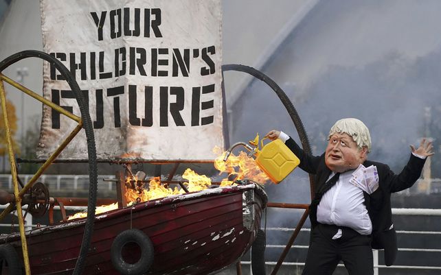 Un activista de la campaña medioambiental Ocean Rebellion vestido como el primer ministro Boris Johnson enciende la vela de un pequeño bote que dice El futuro de sus hijos