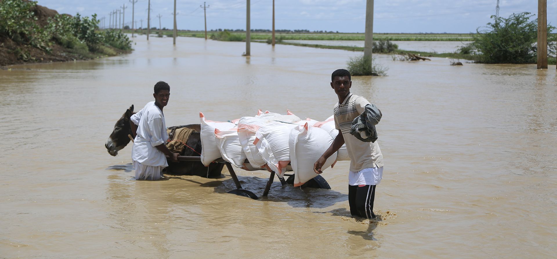 La gente camina por una carretera inundada cerca de la aldea de Aboud en el distrito de El Manaqil, Sudán, el viernes 19 de agosto de 2022.