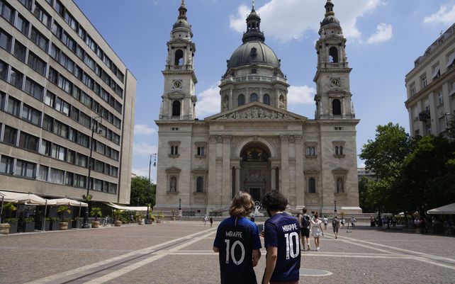 Dos aficionados franceses con camisetas de Kylian Mbappé caminan frente a la Basílica de San Esteban