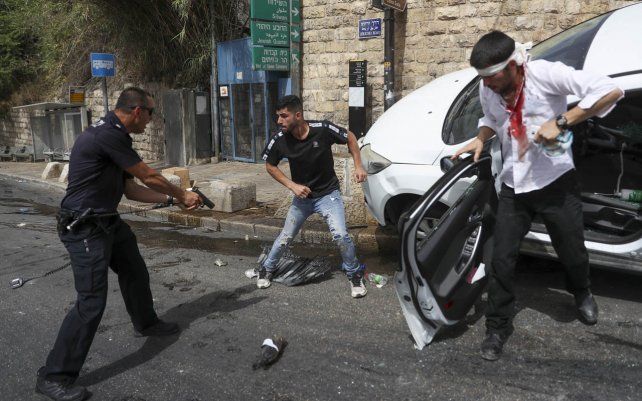 Un oficial de policía israelí apunta con una pistola a un hombre palestino, en el centro, junto a un conductor judío que fue atacado por manifestantes palestinos cerca de la Ciudad Vieja de Jerusalén.