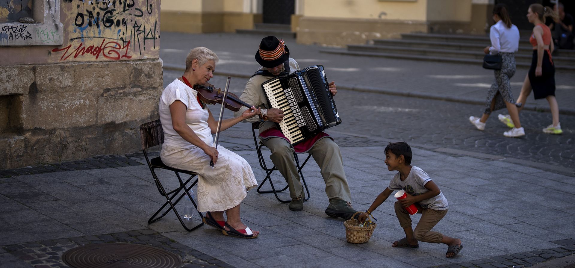 Un niño intenta robar dinero de los músicos callejeros que tocan en el centro de Lviv, Ucrania, el viernes 26 de agosto de 2022.