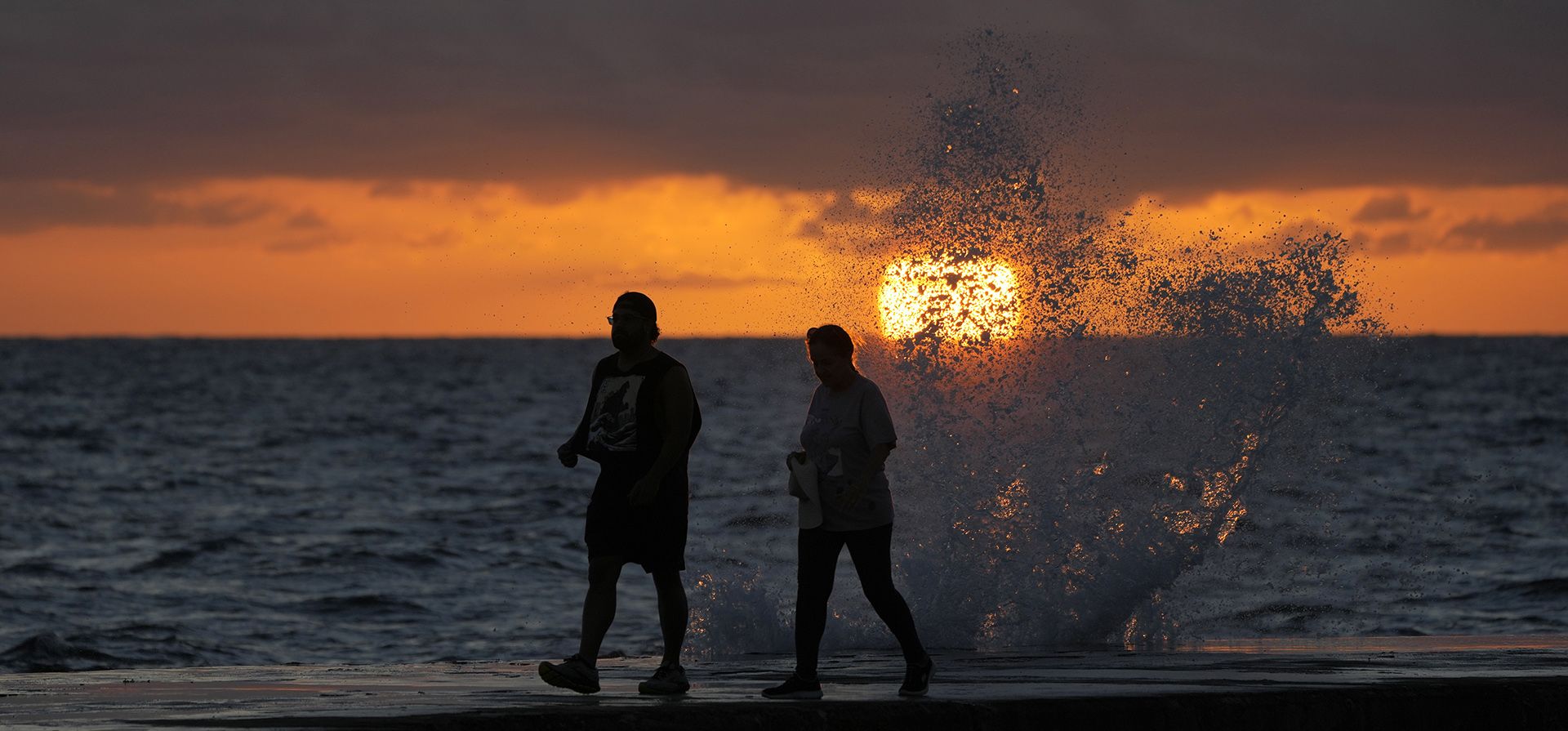 El sol sale sobre el Océano Atlántico mientras las olas rompen cerca de los bañistas que caminan por un embarcadero, el miércoles 7 de diciembre de 2022 en Bal Harbour, Florida (AP Photo/Wilfredo Lee)