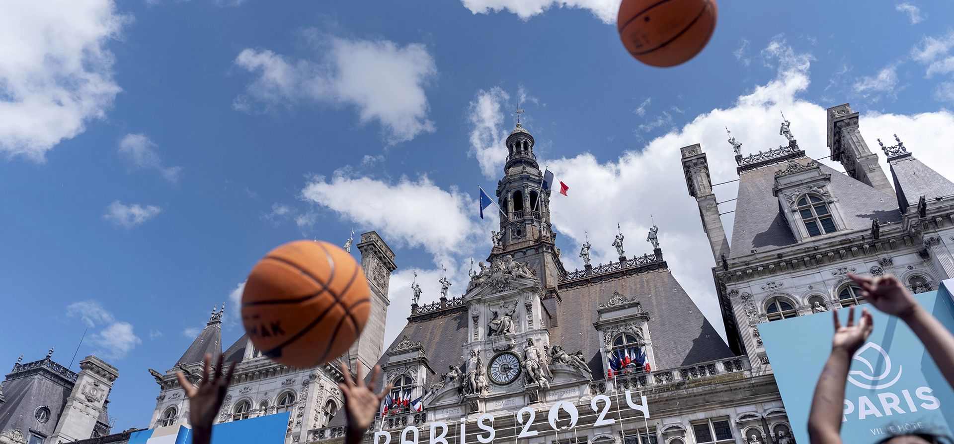 El Hotel de Ville, o ayuntamiento, está decorado para los Juegos Olímpicos de Verano de 2024 mientras los niños lanzan pelotas de baloncesto en una zona de aficionados ubicada en la plaza, el domingo 21 de julio de 2024, en París. Francia. (Foto AP/David Goldman) El Hotel de Ville, o ayuntamiento, está decorado para los Juegos Olímpicos de Verano de 2024 mientras los niños lanzan pelotas de baloncesto en una zona de aficionados ubicada en la plaza, el domingo 21 de julio de 2024, en París. Francia. (Foto AP/David Goldman)