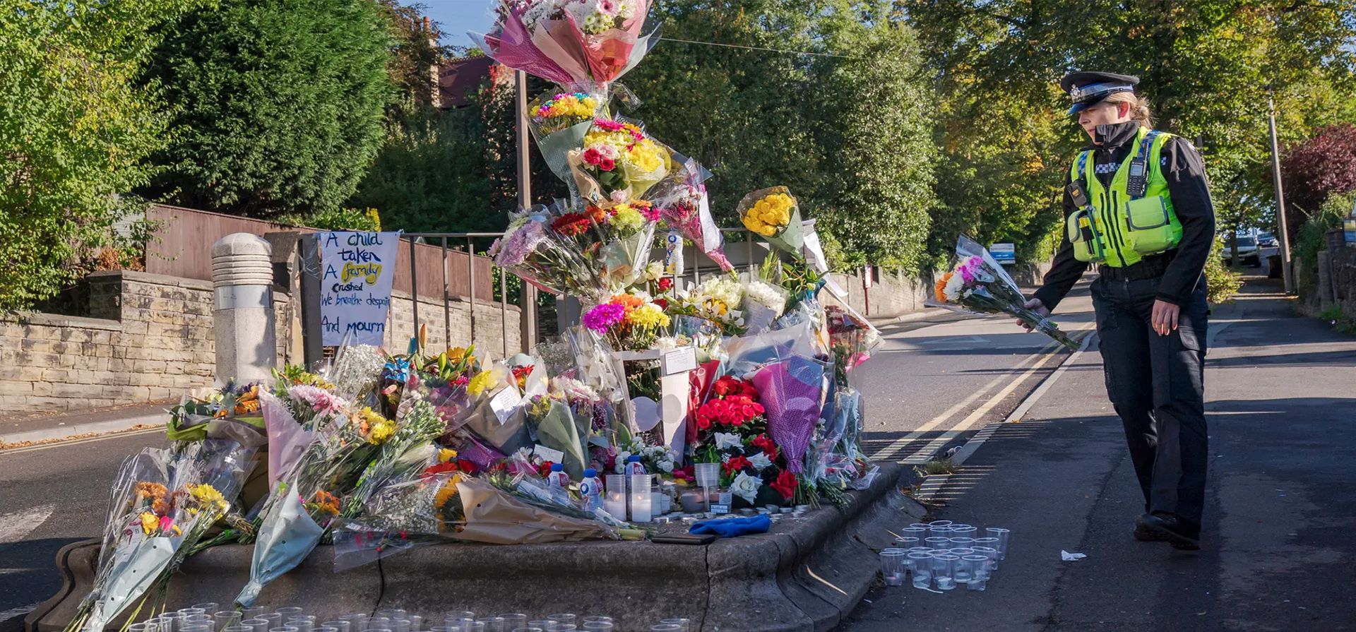 Un oficial de apoyo comunitario de la policía deposita un tributo floral en la escena en Woodhouse Hill donde el escolar de 15 años Khayri McLean fue apuñalado fatalmente frente a su escuela. El adolescente murió en el hospital después del ataque, Huddersfield, Inglaterra. Fotografía: Danny Lawson/PA