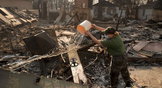 Nancy Belanger vierte agua en la propiedad de un vecino devastada por el incendio en el vecindario Pacific Palisades de Los Ángeles.