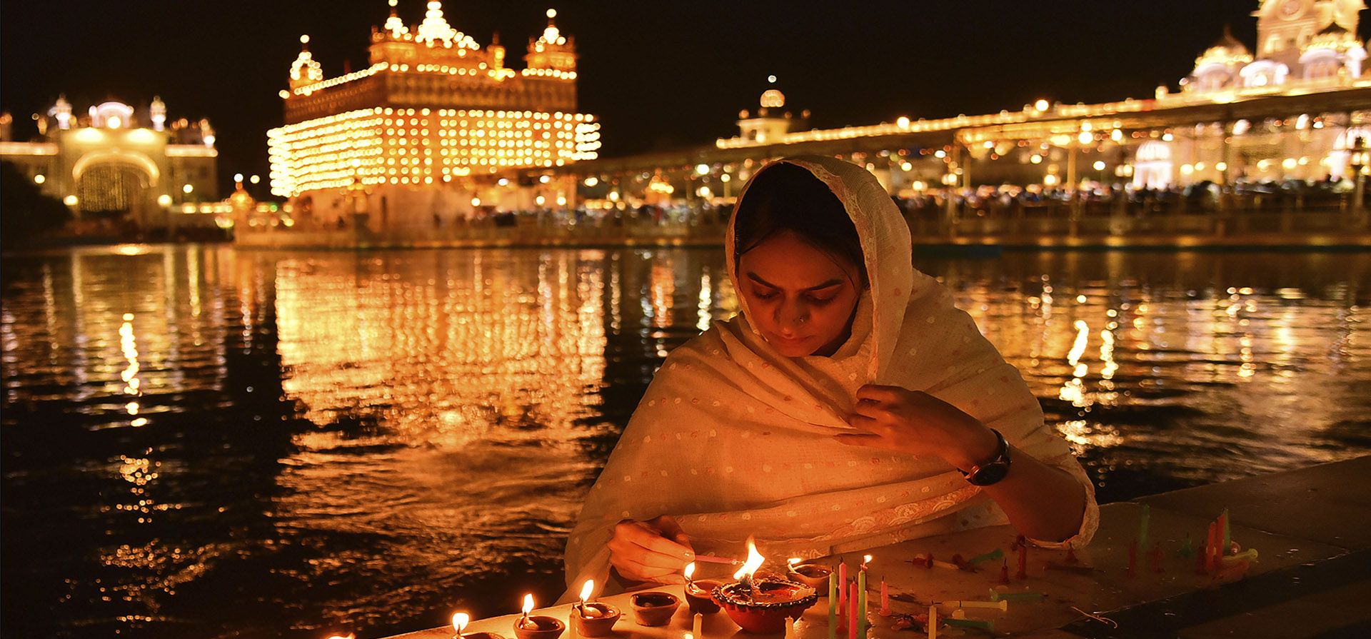 Una devota sij enciende velas en el Templo Dorado iluminado con motivo del aniversario del nacimiento de Guru Nanak, el primer gurú sij y fundador del sijismo, en Amritsar, India, el martes 8 de noviembre de 2022.