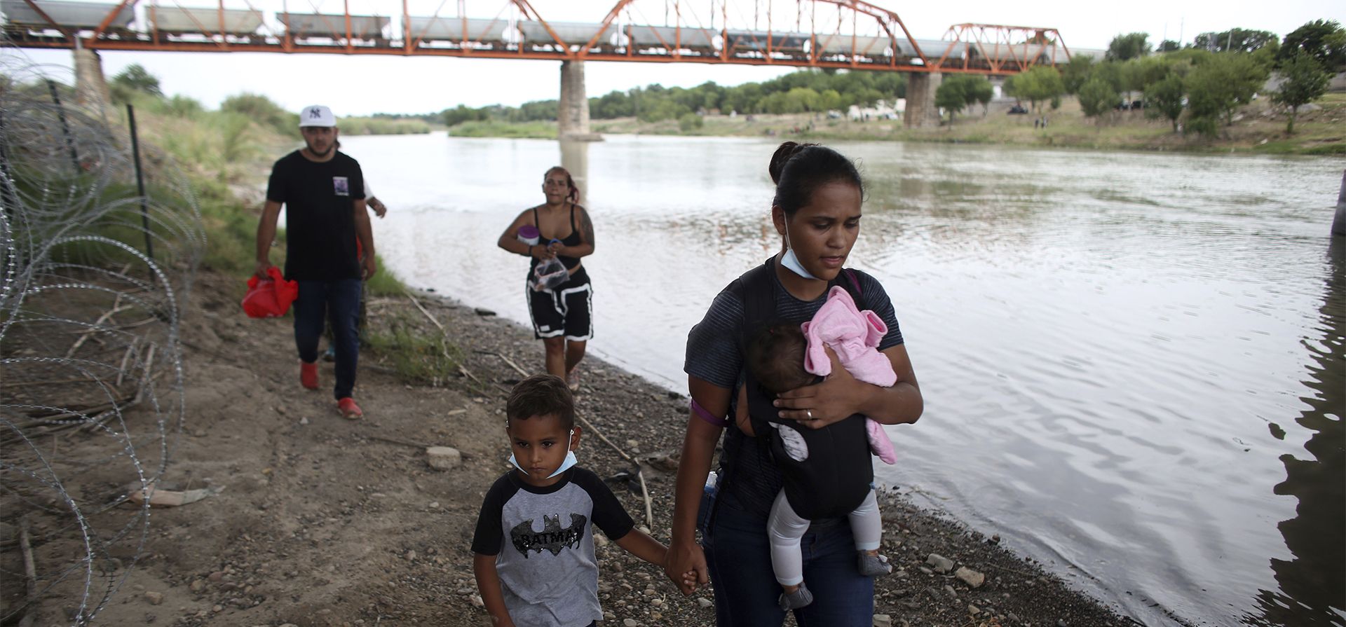 Migrantes caminan por la orilla para ser llevados por la Patrulla Fronteriza después de cruzar el río Grande en Eagle Pass, Texas, el domingo 22 de mayo de 2022.