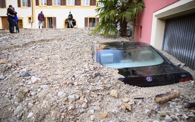Un hombre consuela a su mujer al observar un automóvil&nbsp; enterrado bajo los escombros después de una violenta tormenta en Cressier