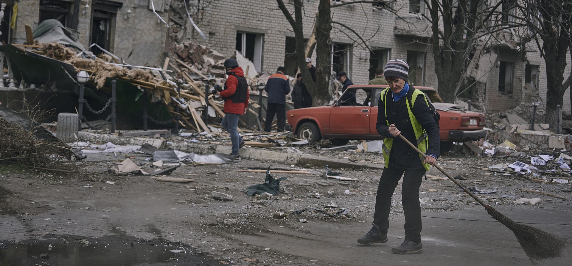 Trabajadores comunales limpian los escombros de la calle frente a un edificio gravemente dañado después de un ataque ruso en Sloviansk, región de Donetsk, Ucrania, el lunes 27 de marzo de 2023. (Foto AP/Libkos)