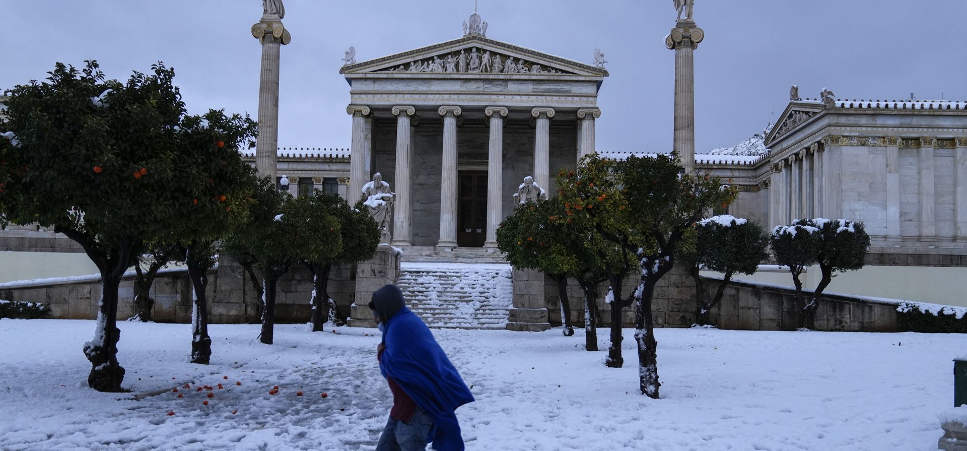 Una persona envuelta en una manta camina sobre la nieve frente a la Academia de Atenas. Una tormenta de nieve de gravedad interrumpió el tráfico aéreo y por carretera el lunes en la capital griega de Atenas y en la vecina ciudad más grande de Turquía, Estambul.
