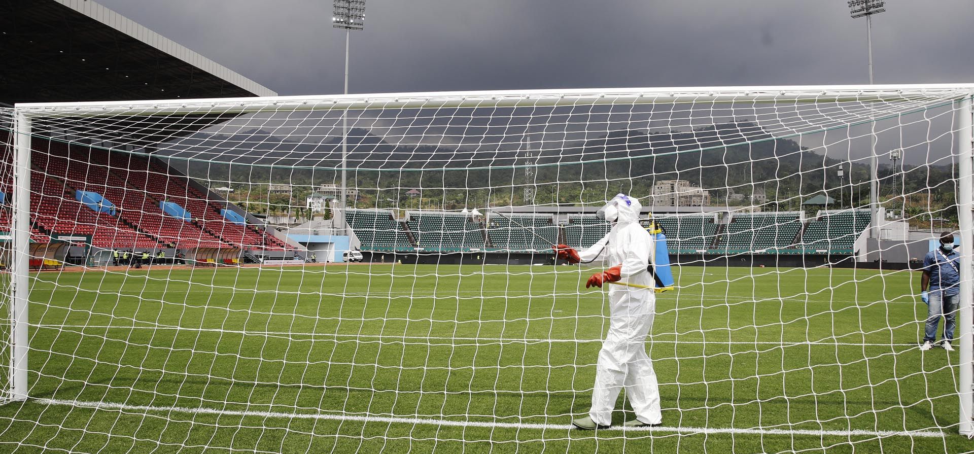 Un funcionario con equipo de protección personal rocía los postes de la portería con spray desinfectante antes del partido de fútbol del grupo F de la Copa Africana de Naciones 2022 entre Túnez y Malí en el estadio Limbe Omnisport en Limbe, Camerún, el miércoles 12 de enero de 2022.
