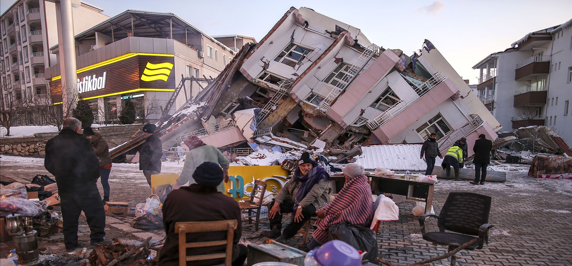 La gente se sienta alrededor de un edificio derrumbado en Golbasi, en la provincia de Adiyaman, en el sur de Turquía, el jueves 9 de febrero de 2023. El gobierno turco ha tentado durante años al destino al no hacer cumplir los códigos de construcción modernos al mismo tiempo que lo permitía, y en algunos casos, alentadores: un auge inmobiliario en áreas propensas a terremotos, según expertos en geología e ingeniería que emitieron repetidas advertencias. (Foto AP/Emrah Gurel)