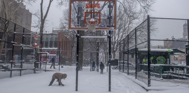Niños juegan en una cancha de baloncesto cubierta de nieve cerca de Washington Square. 