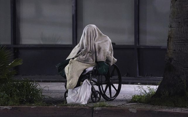 Una persona sin hogar sentada en una silla de ruedas bajo un clima lluvioso en Sunset Blvd.