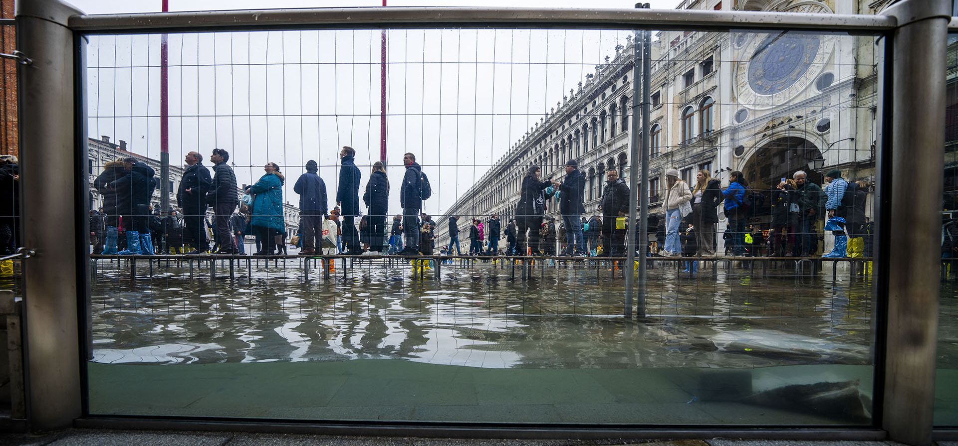 Turistas y residentes caminan sobre pasarelas durante una marea marina de alrededor de 97 centímetros para cruzar la Plaza de San Marcos inundada en Venecia, en el norte de Italia, donde las barreras de vidrio recientemente instaladas evitan que el agua del mar inunde la La emblemática basílica de San Marcos de 900 años de antigüedad. La Plaza de San Marcos es el área de la ciudad más baja y con frecuencia termina bajo el agua durante condiciones climáticas extremas. (Foto AP/Domenico Stinellis)