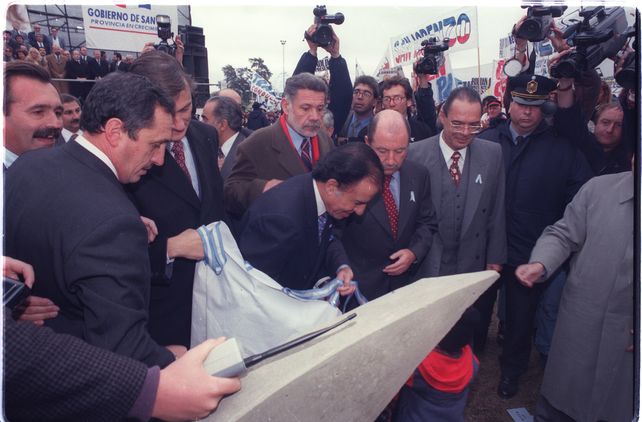 20 de junio de 1997. El presidente Menem descubre la piedra fundamental del puente en la cabecera de Rosario.&nbsp; Y promete que esta obra del puente “será una realidad” y que en 1999 cuando termine su gobierno dejará a “la Argentina entre los diez mejores países de al tierra”. Lo primero lo cumplió