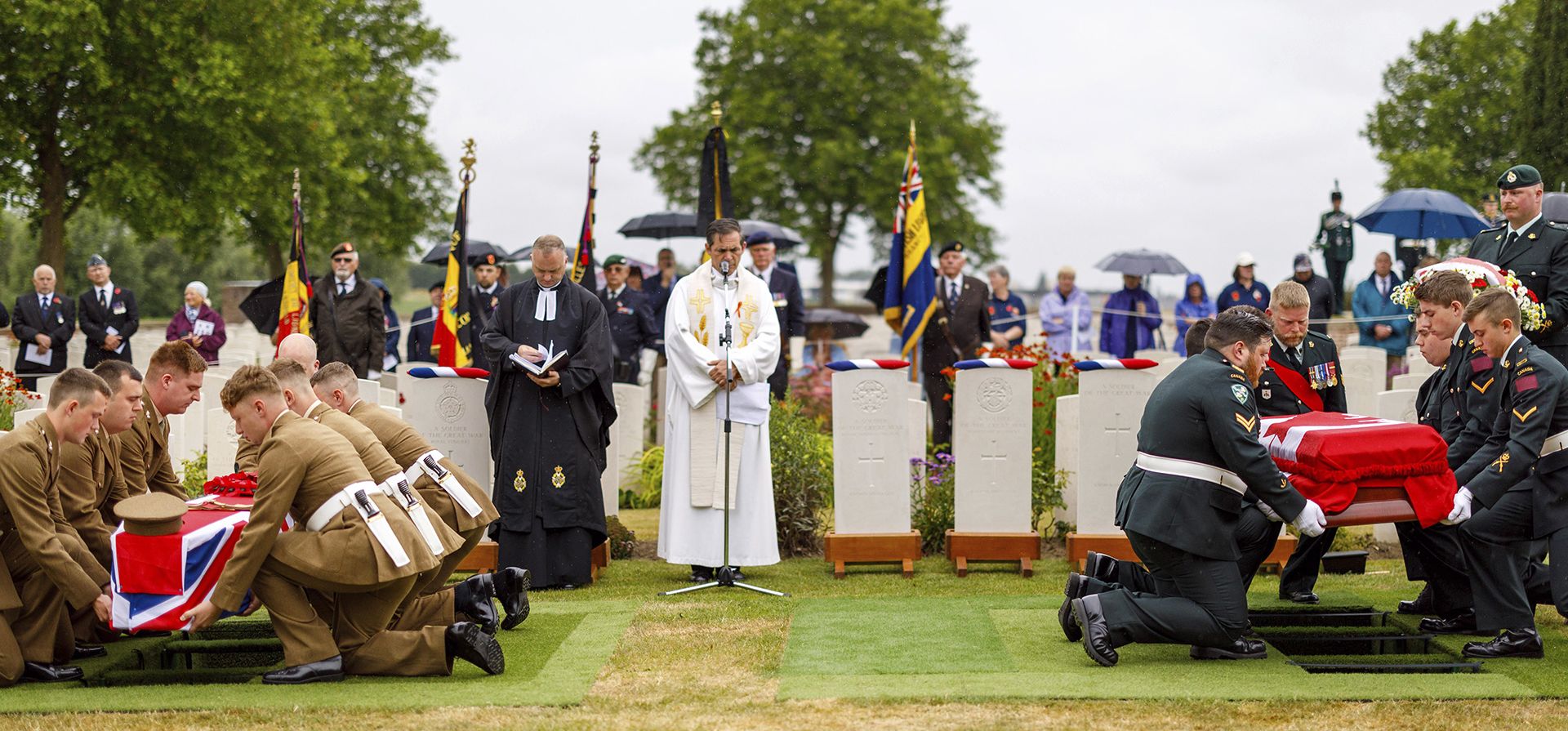 Los portadores del féretro del regimiento, a la izquierda, y los portadores del féretro del ejército canadiense, a la derecha, bajan los ataúdes de un soldado británico no identificado de la Primera Guerra Mundial y el soldado canadiense John Lambert del Regimiento de Terranova, de la Primera Guerra Mundial,  durante una ceremonia de entierro con todos los honores militares en la Guerra de la Commonwealth de Granjas Irlandesas Cementerio Graves en Ypres, Bélgica, el jueves 30 de junio de 2022. 