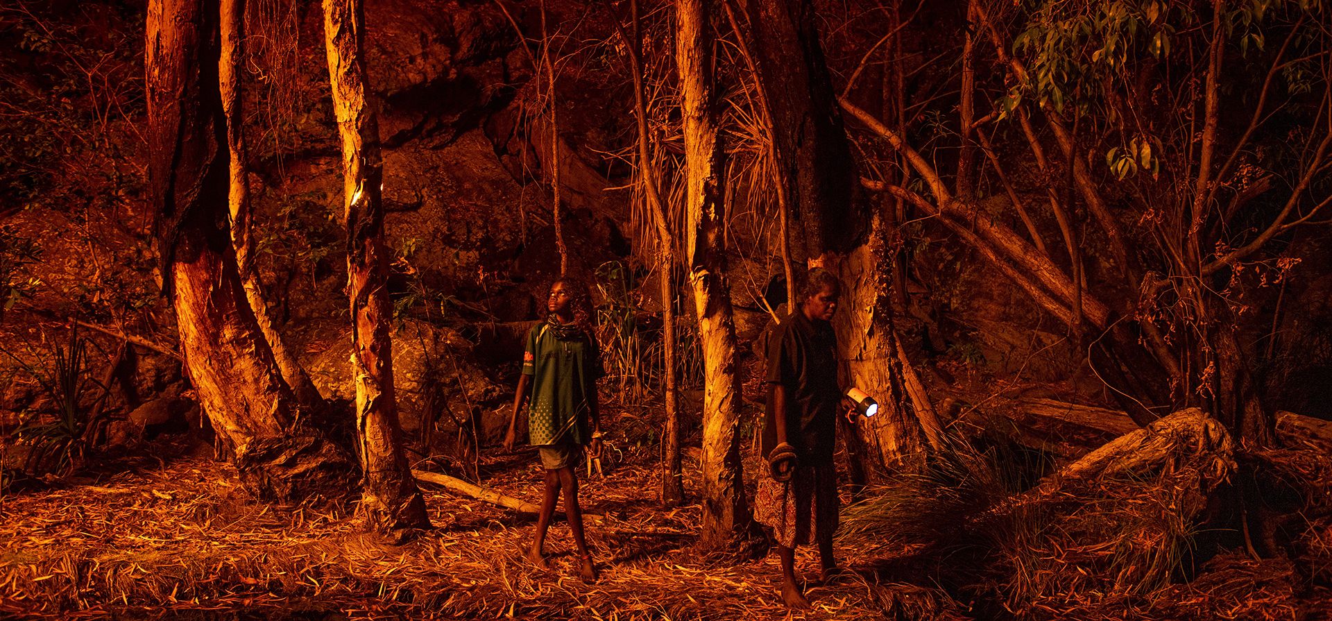 Premio World Press Photo Story Of The Year de Matthew Abbott para National Geographic Magazine/Panos Pictures, titulada Saving Forests With Fire, muestra a Stacey Lee, de 11 años, a la izquierda, camina entre árboles buscando una fuente de luz natural para ayudar a cazar serpientes, en Djulkar, Arnhem Land, Australia, el 22 de julio de 2021. (Matthew Abbott para National Geographic/Panos Pictures/World Press Photo vía AP)