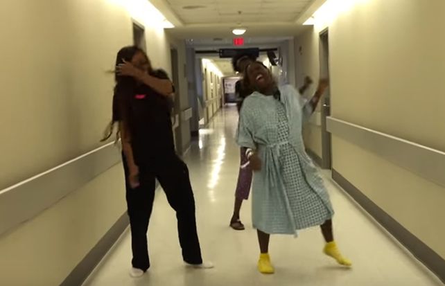 La mujer que está a punto de parir y sus dos amigas bailan en un pasillo de un hospital.
