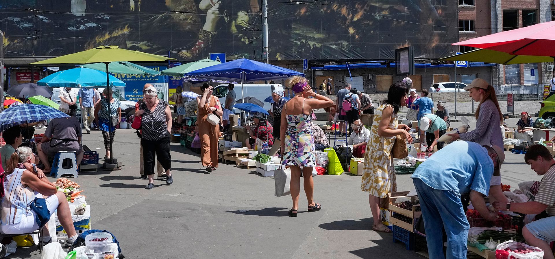 Gente compra comida en un mercado improvisado rodeado de edificios dañados cubiertos por una obra de un artista callejero, junto a un gran mercado destruido hace poco por misiles rusos en Kiev, Ucrania, el lunes 22 de junio de 2026. (AP Foto/Efrem Lukatsky) Gente compra comida en un mercado improvisado rodeado de edificios dañados cubiertos por una obra de un artista callejero, junto a un gran mercado destruido hace poco por misiles rusos en Kiev, Ucrania, el lunes 22 de junio de 2026. (AP Foto/Efrem Lukatsky)