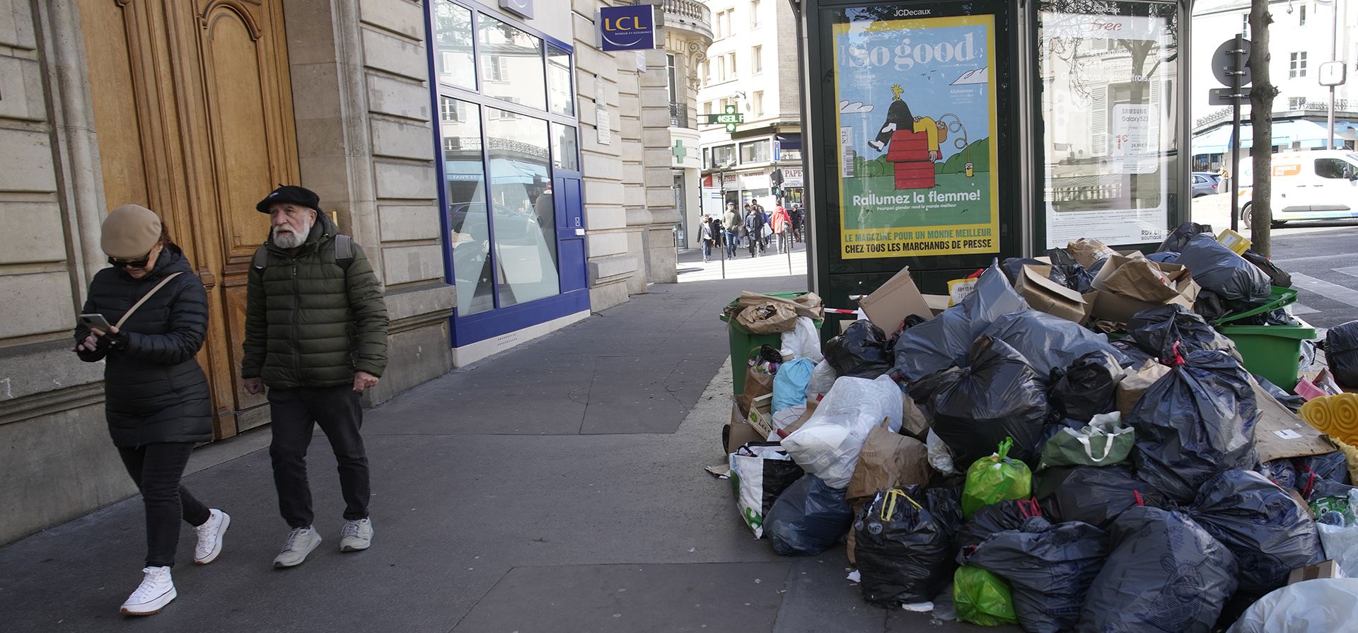 Una pareja pasa junto a una pila de bolsas de basura sin recoger, el lunes 27 de marzo de 2023 en París. El presidente Emmanuel Macron inflamó la ira pública al enviar su ya impopular plan para aumentar la edad de jubilación en dos años, de 62 a 64, a través del parlamento sin votación. (Foto AP/Christophe Ena)