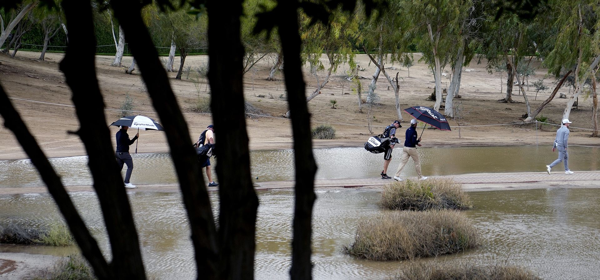 Los jugadores caminan por el hoyo 17 bajo la lluvia durante el segundo día del Dubai Desert Classic, en Dubái, Emiratos Árabes Unidos, el viernes 27 de enero de 2023. (Foto AP/Kamran Jebreili)
