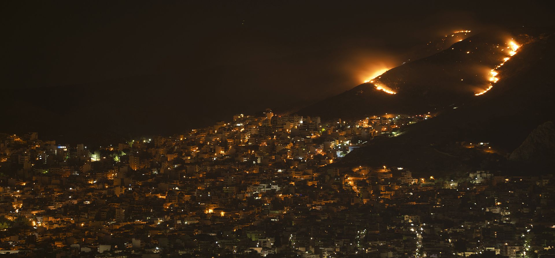 El fuego arde en una colina cerca de Korydallos, al oeste de Atenas, la madrugada del jueves 30 de junio de 2022. Decenas de bomberos luchan contra un incendio forestal al oeste de Atenas. No se han reportado lesiones. 