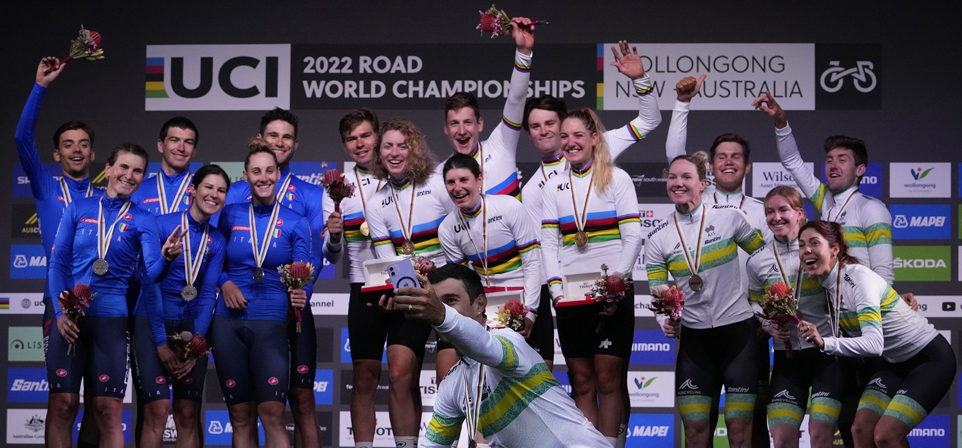 Michael Matthews, de Australia, usa un teléfono para fotografiar a los equipos que se ubicaron en el relevo mixto de contrarreloj por equipos en el campeonato mundial de ciclismo en ruta en Wollongong, Australia, el miércoles 21 de septiembre de 2022. Suiza, en el centro de la defensa, ganó el oro , Italia, a la izquierda, se llevó la plata y Australia ganó el bronce.