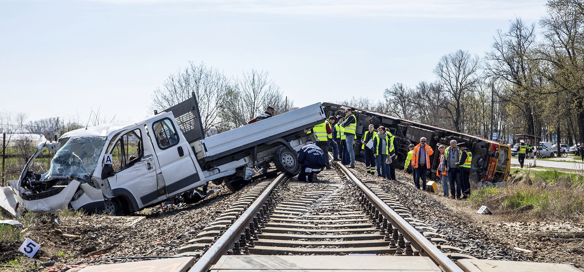 Oficiales de policía y bomberos inspeccionan la escena después de que un tren de pasajeros que viajaba en la línea Szentes - Hodmezovasarhely se descarriló y cayó en una zanja a 60 metros del lugar del impacto en Mindszent, Hungría, el martes 15 de abril de 2022. Cinco personas murieron y más de diez resultaron heridos cuando una camioneta chocó contra un tren.
