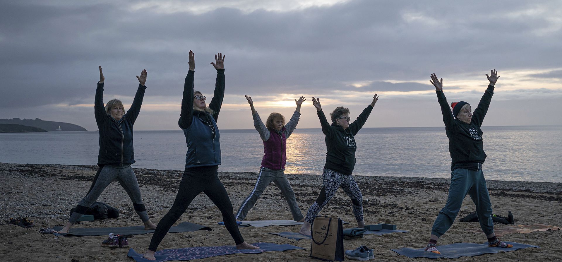 La gente practica yoga en la playa de Gyllyngvase, mientras sale el sol en Cornualles, donde persiste un clima más templado y las temperaturas se mantienen muy por encima del punto de congelación a lo largo de la costa de Cornualles, en Falmouth, Gran Bretaña, el jueves 9 de febrero de 2023. (Ben Birchall/PA vía AP)