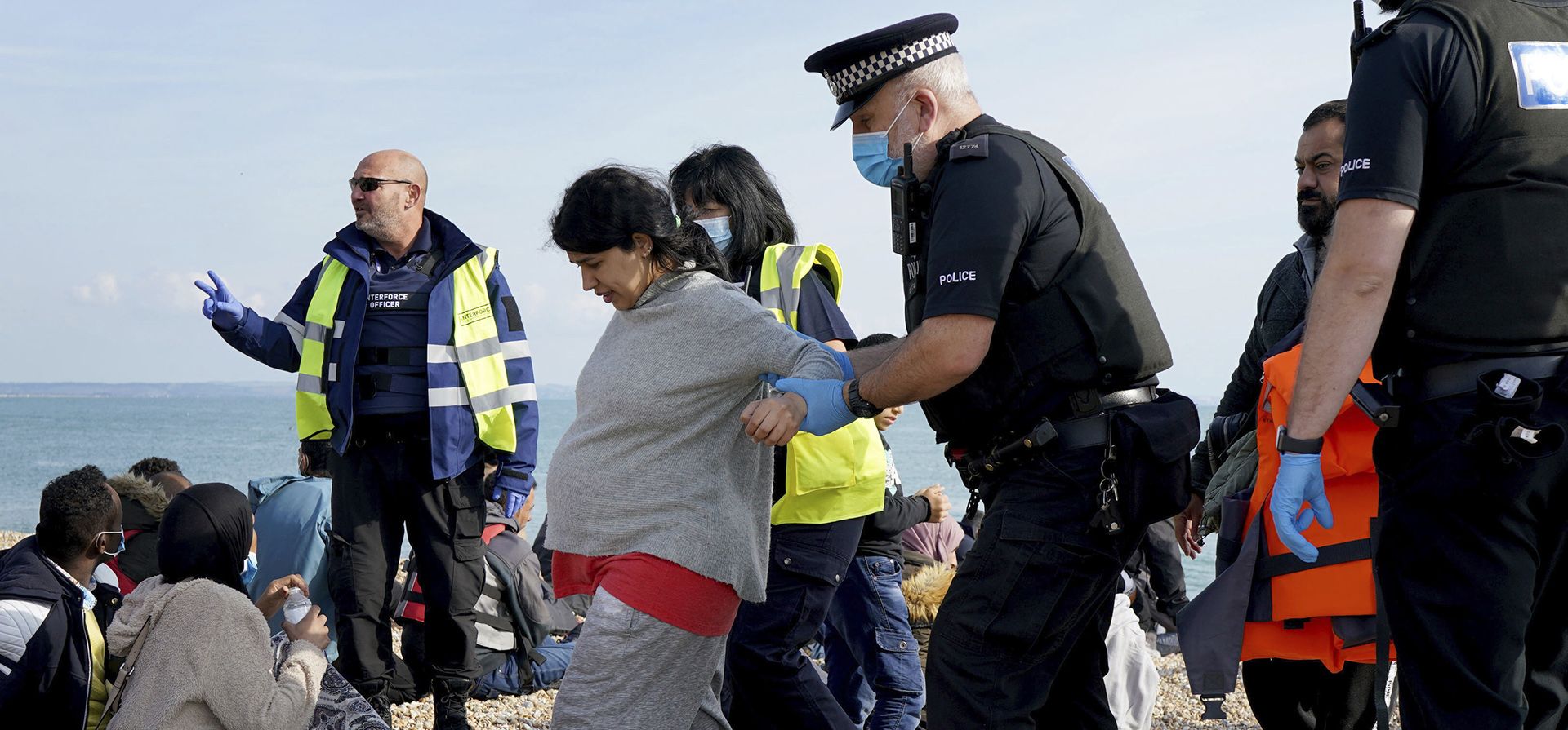 Agentes de policía ayudan a una mujer con un embarazo avanzado mientras un grupo de personas que se cree que son inmigrantes caminan por la playa en Dungeness, Kent, Inglaterra, luego de ser rescatadas en el Canal por el RNLI durante un incidente con un bote pequeño, el jueves 22 de septiembre de 2022.
