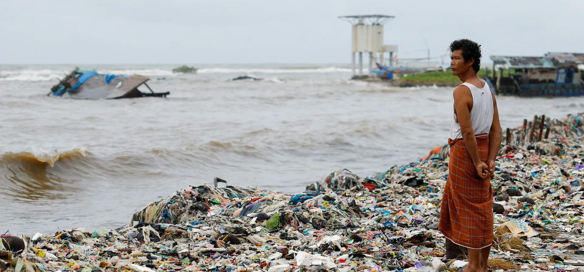 Un aldeano se encuentra entre el plástico y los desechos domésticos en una playa mientras las mareas altas lo arrastran hasta la orilla, en la provincia de Banten, Teluk, Indonesia. Fotografía: Willy Kurniawan/Reuters Un aldeano se encuentra entre el plástico y los desechos domésticos en una playa mientras las mareas altas lo arrastran hasta la orilla, en la provincia de Banten, Teluk, Indonesia. Fotografía: Willy Kurniawan/Reuters