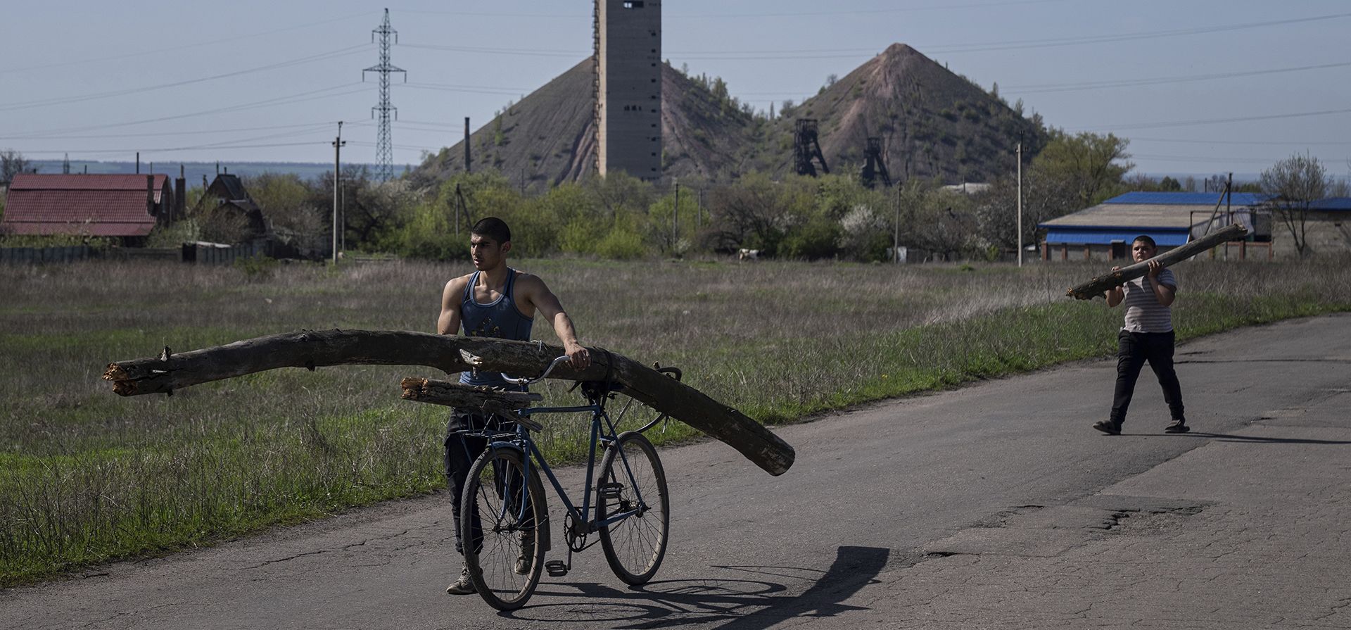 Un hombre lleva una la rama de un árbol sobre su bicicleta frente a una mina de carbón en Toretsk, este de Ucrania, el martes 26 de abril de 2022.
