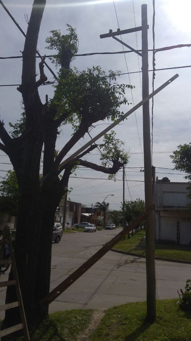 Vecinos sostienen un poste de luz con una escalera y palos para que no se caiga