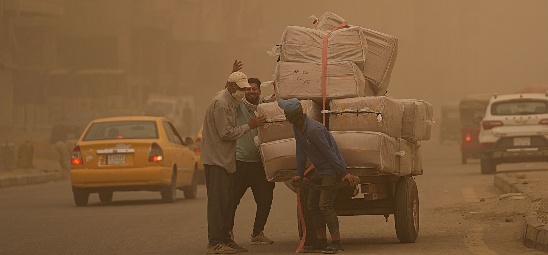 Personas empujan un carro durante una tormenta de arena en Bagdad, Irak, el lunes 23 de mayo de 2022.