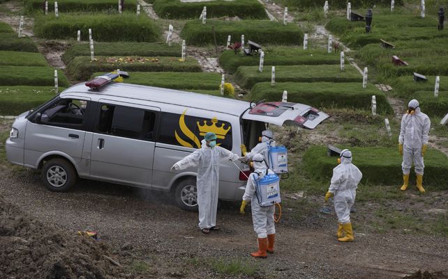 Un trabajador rocía a un compañero con desinfectante después del entierro de una persona que presuntamente murió por coronavirus en un cementerio en Medan