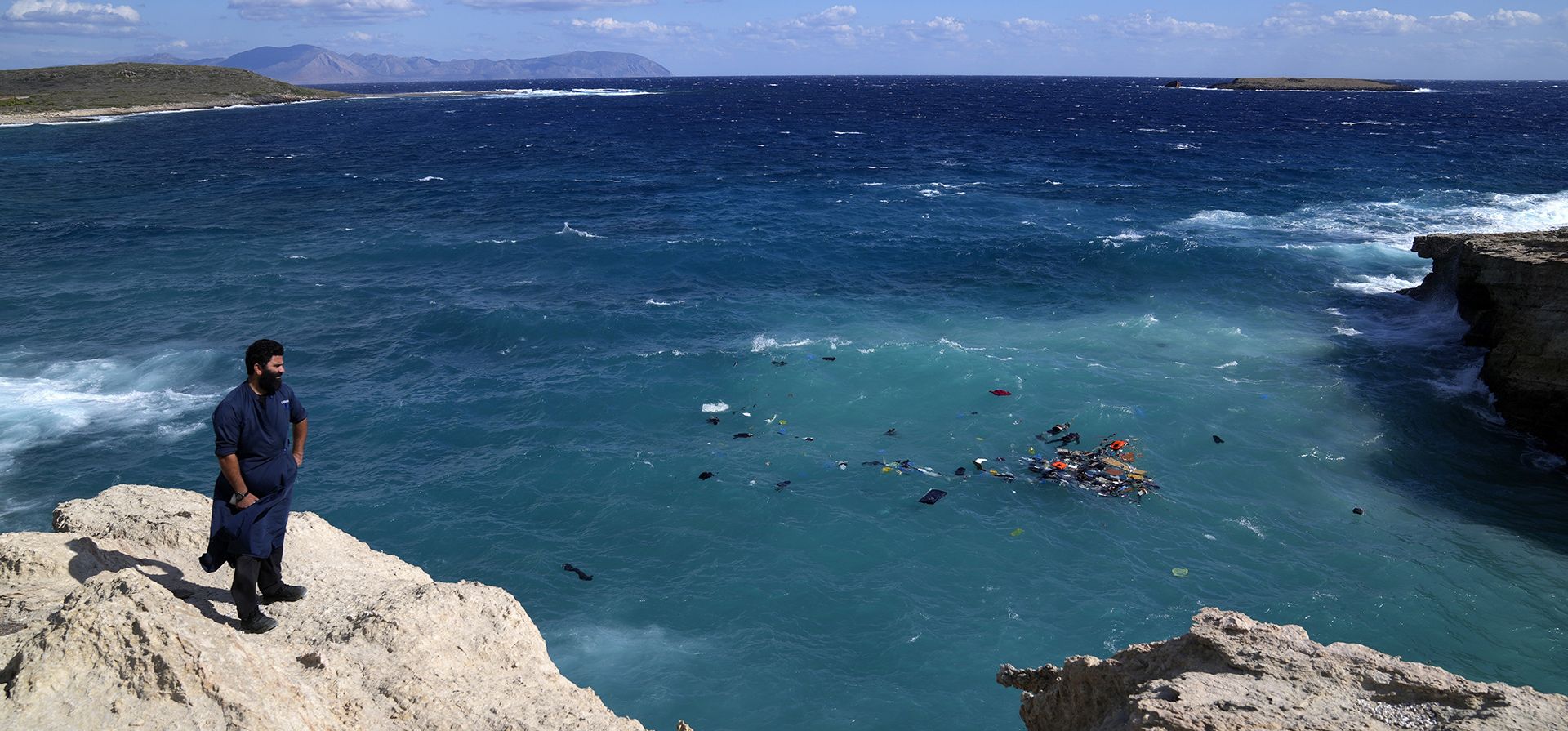 Un residente local se para en un acantilado mientras se ven cuerpos junto a escombros flotantes después de que un velero que transportaba migrantes se estrellara contra las rocas y se hundiera frente a la isla de Kythira, en el sur de Grecia, el jueves 6 de octubre de 2022.