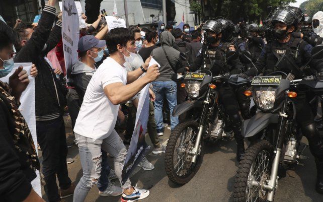 Refugiados afganos que viven en Indonesia gritan consignas frente a agentes de policía durante una manifestación frente al edificio que alberga la oficina de representación del ACNUR en Yakarta, Indonesia, el martes 24 de agosto de 2021.