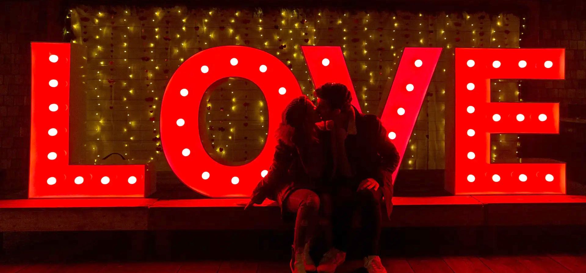 Una pareja se besa junto a un cartel de amor iluminado en el parque del puente colgante de Capilano, Vancouver, Canada. 