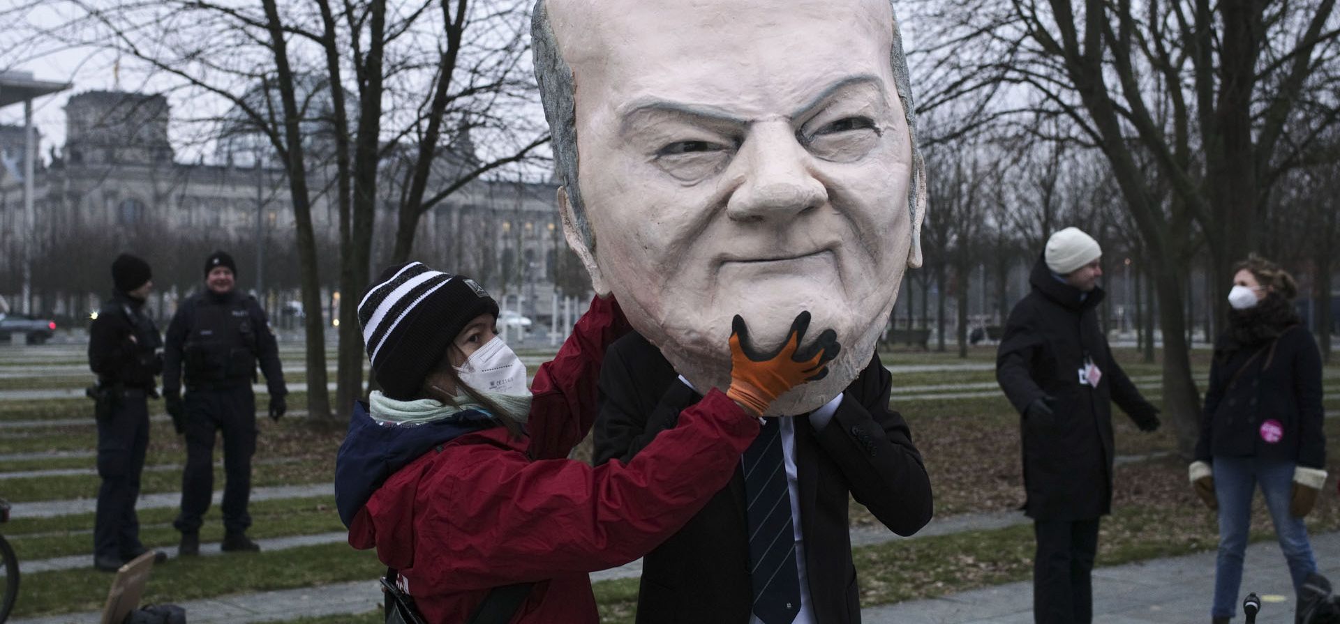 Un activista ayuda a otro activista a ponerse una máscara del canciller alemán Olaf Scholz antes de una protesta contra la política climática cerca de la Cancillería en Berlín, Alemania, el martes 11 de enero de 2022.
