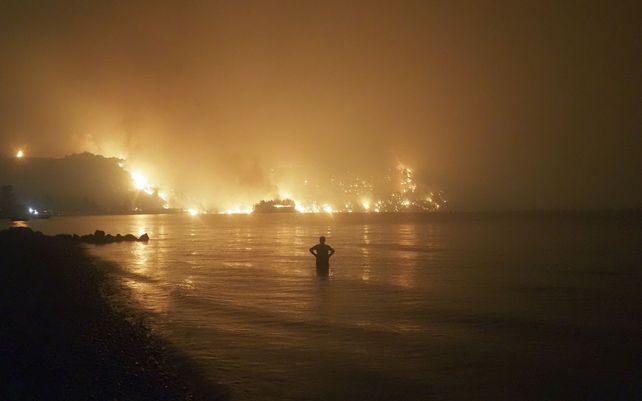 Un hombre observa las llamas mientras un incendio forestal se acerca a la playa de Kochyli