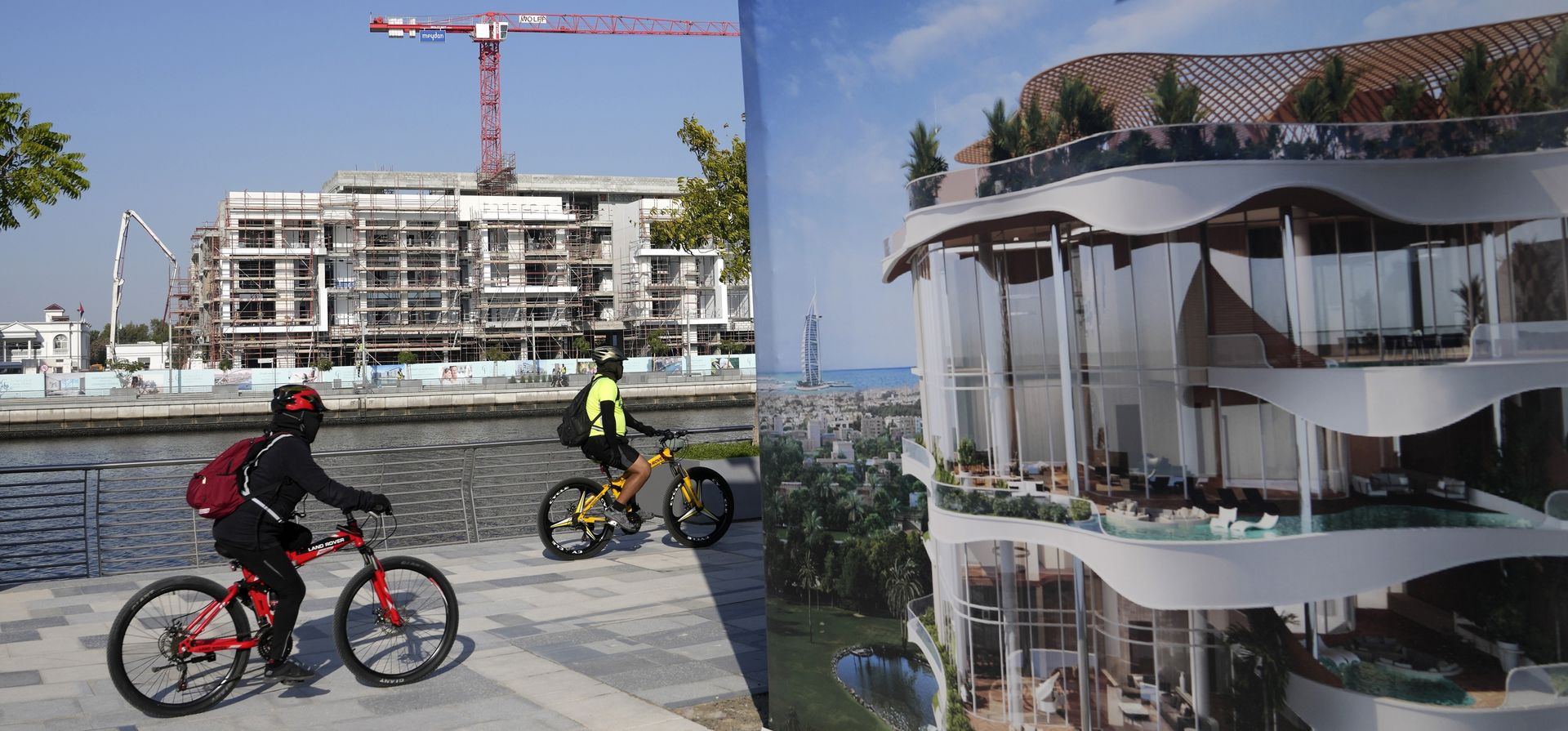 Ciclistas recorren el canal de agua de Dubái mientras pasan junto a una valla publicitaria residencial y un proyecto residencial en construcción en Dubái, Emiratos Árabes Unidos. (Foto AP/Kamran Jebreili)