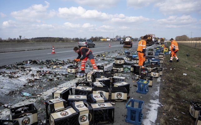 Empleados del departamento de mantenimiento de carreteras limpian la calzada después de que un accidente con un camión de bebidas la obstaculizaran con cajas y envases rotos, en Neumuenster, Alemania.