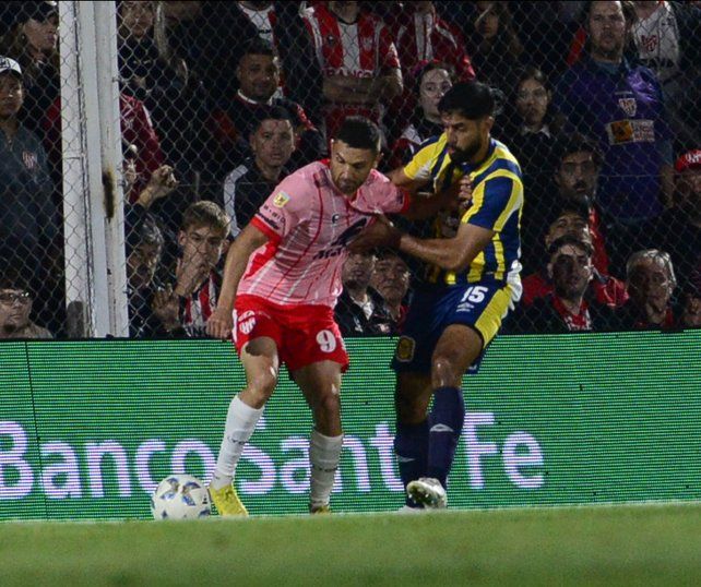 Adrián Martínez aguanta la pelota como puede mientras forcejea con el aguerrido defensor canalla Mallo.