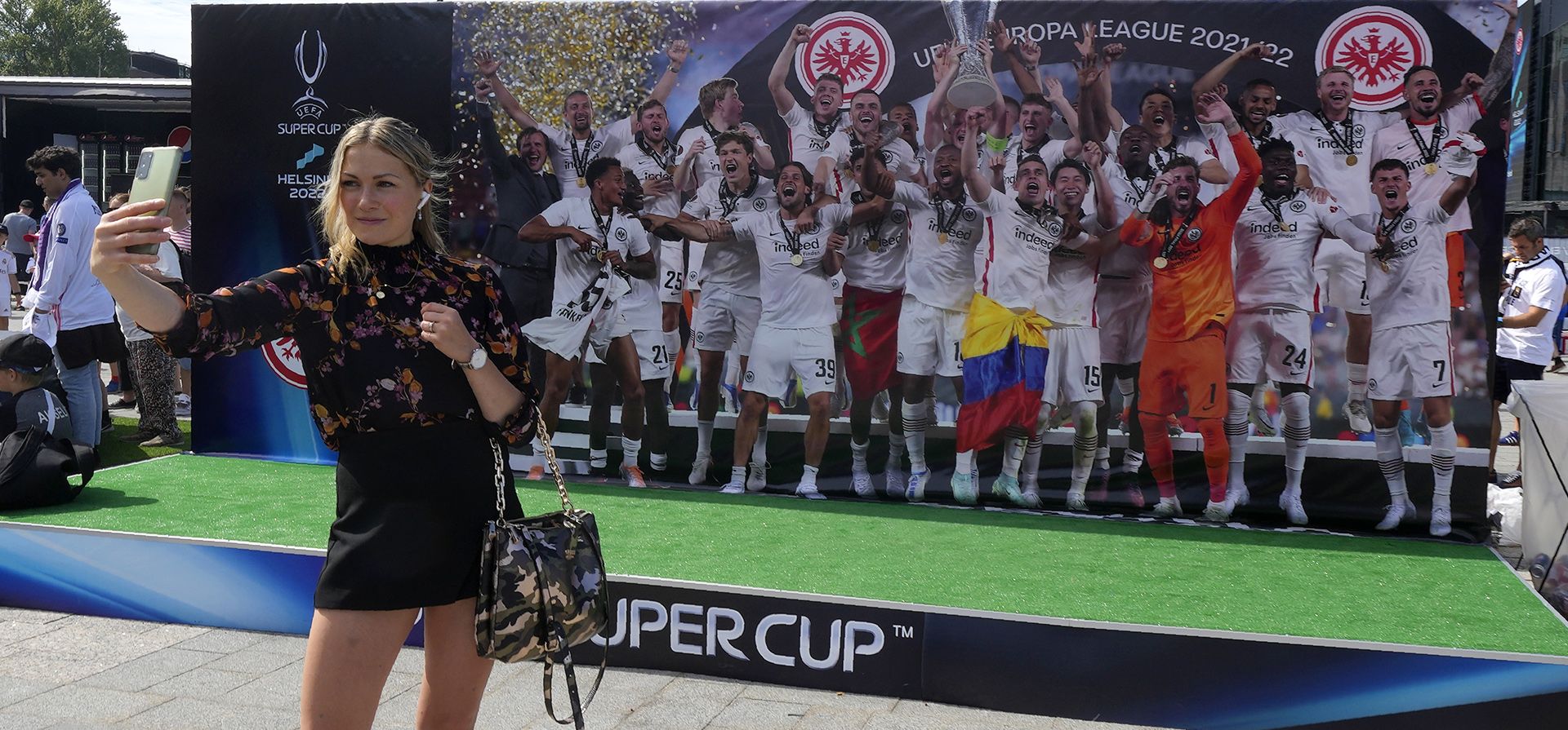 Una joven se toma una selfie frente a una foto gigante del equipo Eintracht Frankfurt en el centro de Helsinki, Finlandia, el miércoles 10 de agosto de 2022. El Real Madrid jugará este miércoles contra Eintracht Frankfurt en la final de la Supercopa de la UEFA.