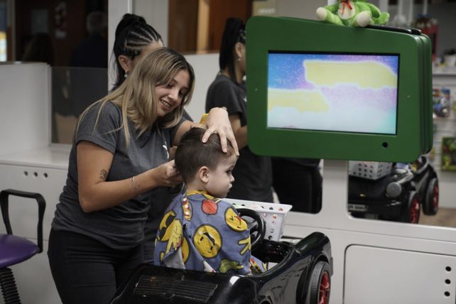 Los chicos disfrutan de los videojuegos mientras un peluquero se encarga de su cabello.
