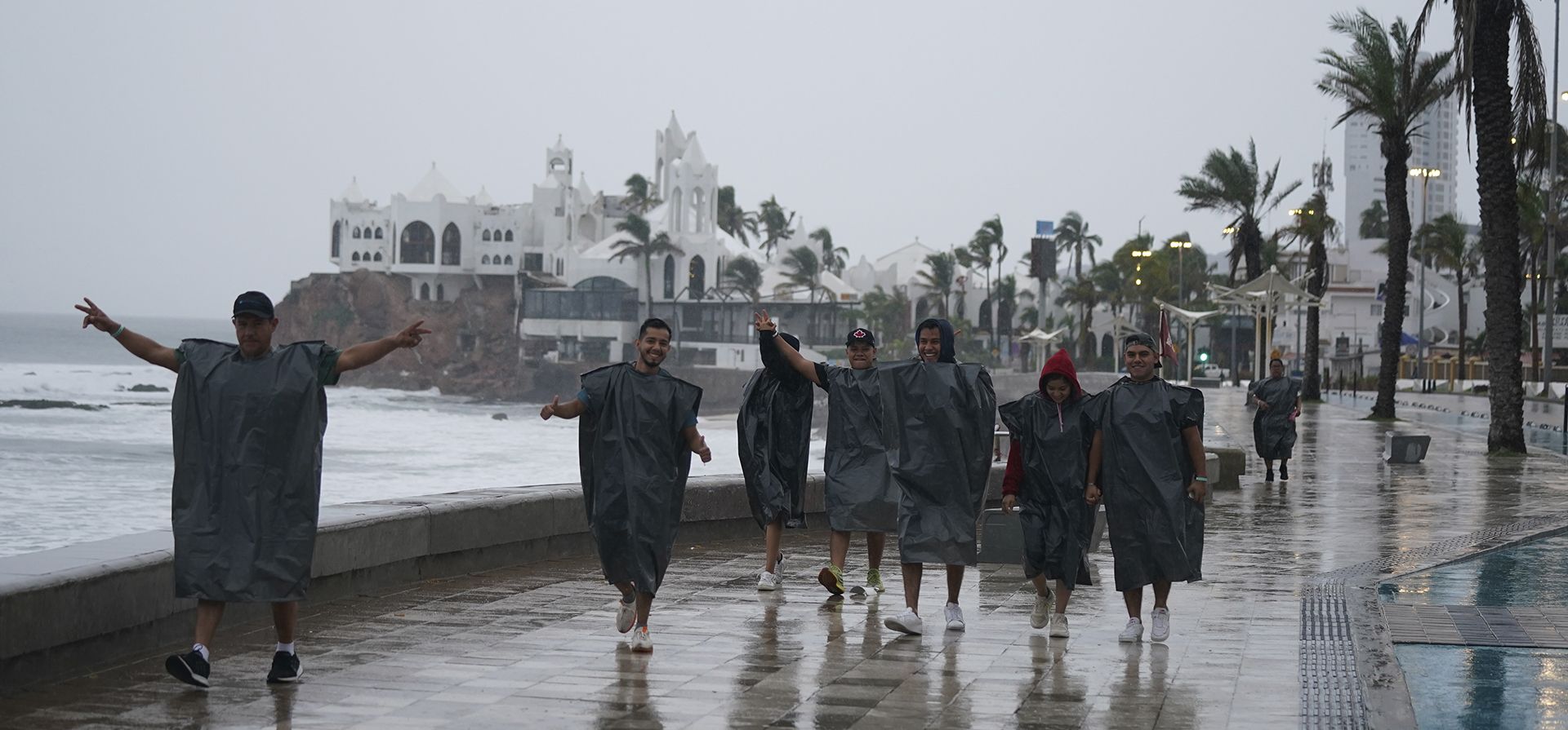 Turistas de Culiacán, México, con bolsas de plástico, bromean con la cámara mientras caminan por la costa de Mazatlán, México, la madrugada del lunes 3 de octubre de 2022, cuando se acerca el huracán Orlene. La tormenta se dirige a la costa noroeste del Pacífico de México entre Mazatlán y San Blas.