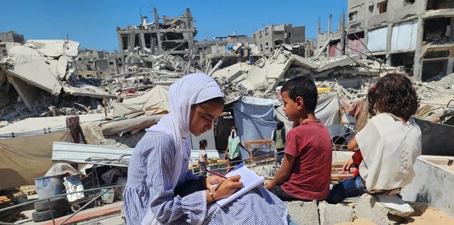 Los estudiantes hacen los deberes después de las clases en su escuela de campaña, construida sobre los escombros de la casa destruida del profesor, Khan Younis, Gaza. Fotografía: Anadolu/Getty Images