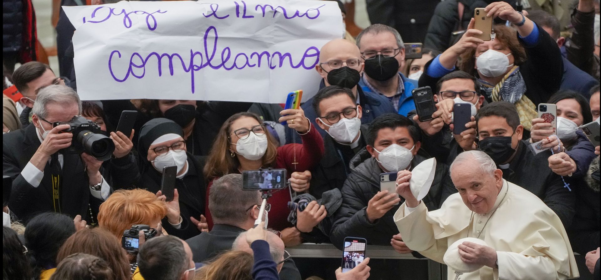 Pope Francisco se pone un gorro que acaba de recibir mientras camina junto a un cartel en italiano que dice: